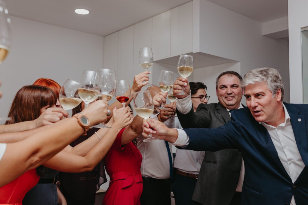 Group of people in business attire toasting with wine glasses in a modern room, celebrating together.