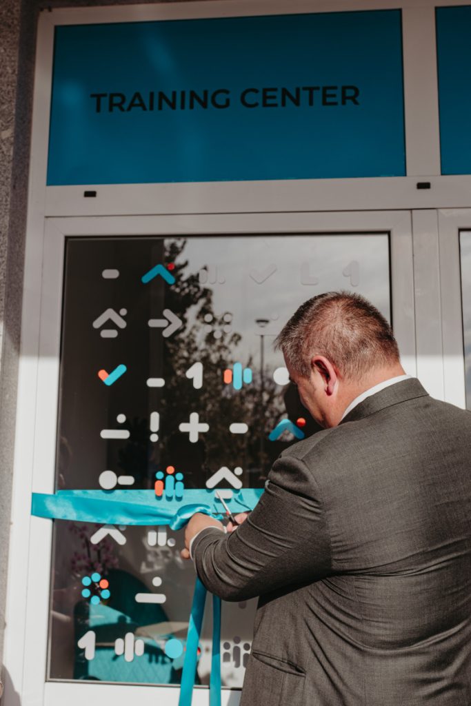 Man in a suit cuts a blue ribbon in front of a glass door labeled Training Center