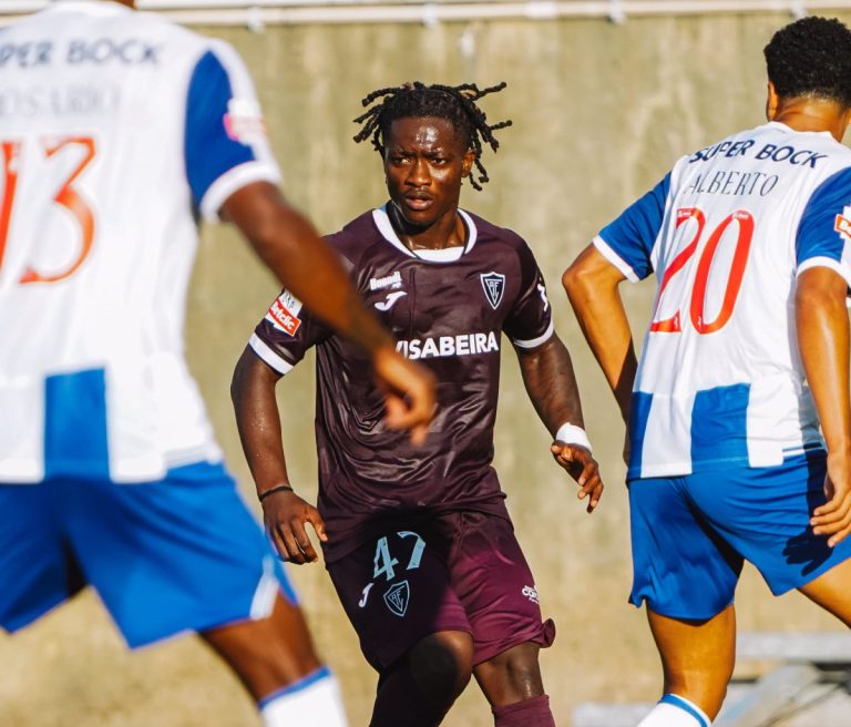 Soccer player in a maroon kit with number 47 controls the ball as two white-and-blue opponents challenge him.