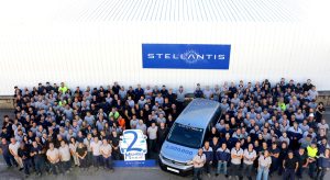 Large group of Stellantis employees posing outside a white industrial building with a blue Stellantis sign above them.