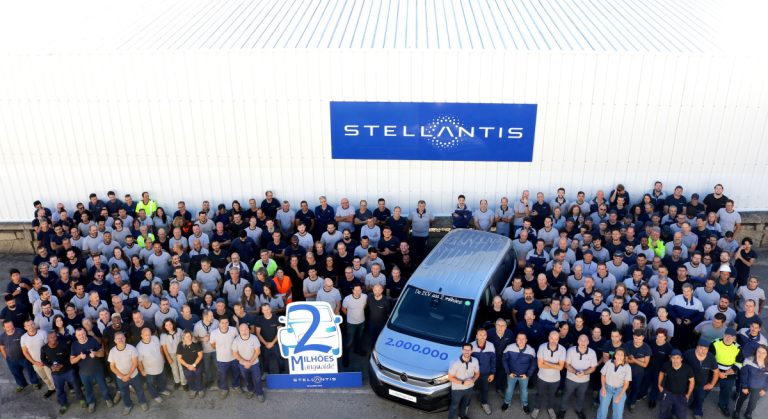 Large group of Stellantis employees posing outside a white industrial building with a blue Stellantis sign above them.