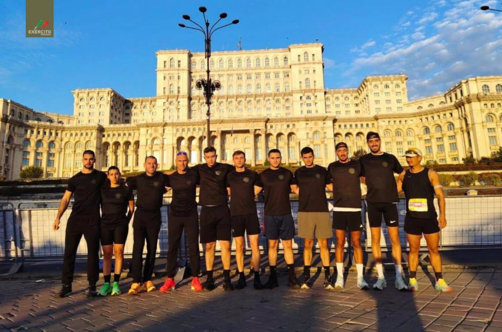 Group of ten runners in black athletic outfits standing arm-in-arm in front of a large historic building; logo with 'EXÉRCITO' top-left corner visible.