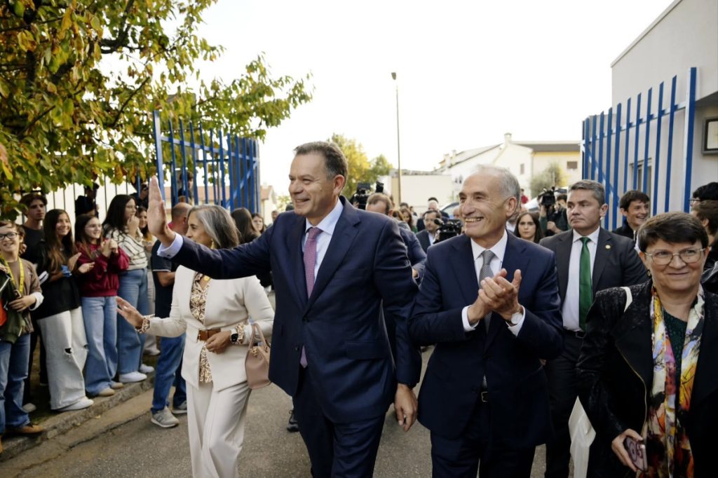 Two men in suits greet a crowd at an outdoor event, with supporters lining the street and clapping.
