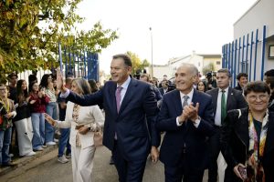 Two men in suits greet a crowd at an outdoor event, with supporters lining the street and clapping.