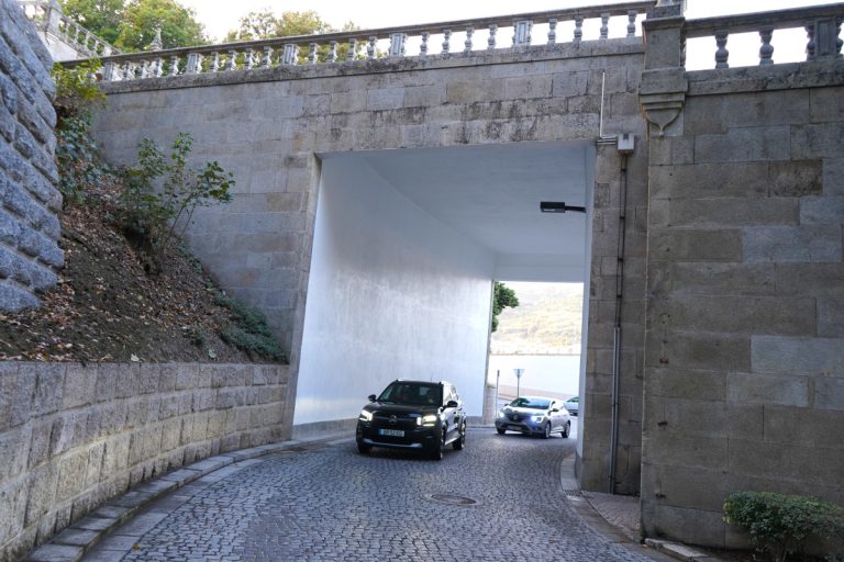 Black SUV driving through a stone tunnel on a cobblestone street, with a white car following behind.
