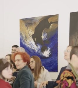 A busy art gallery scene with a group of people gathered near a large blue-and-gold painting featuring a dark silhouette riding a wave.